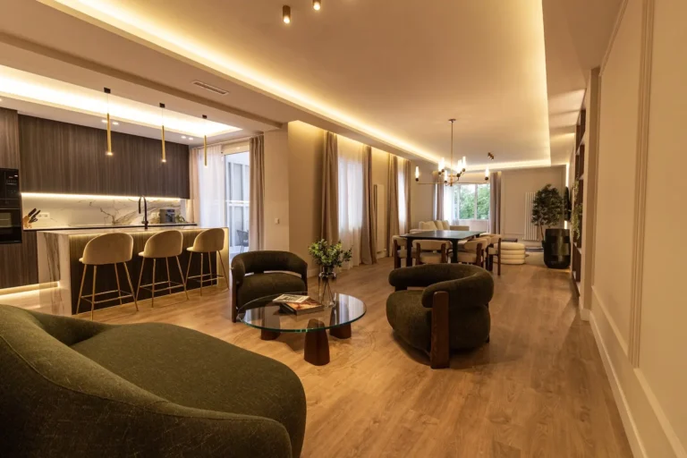 Amplia y moderna sala de estar de planta abierta con cocina con taburetes de bar, mesa de comedor, tumbonas y grandes ventanales que dejan entrar la luz natural.